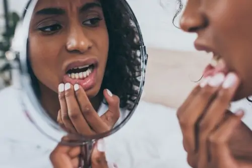 woman with tooth pain examines her teeth in mirror